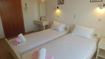 A hotel room with two beds, a wooden door, a small desk, and a mirror.