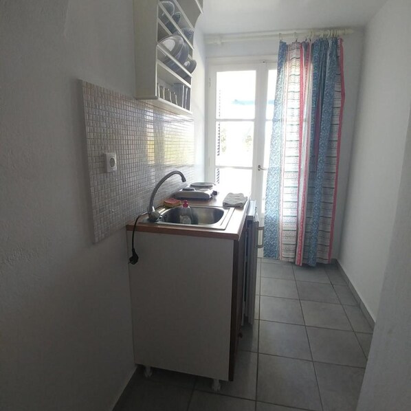 A compact kitchen with a sink, a tiled backsplash, and a window with curtains. - Oasis (Paros)