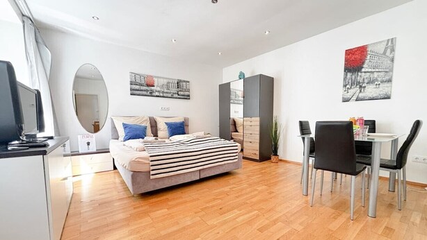 A modern room with a bed, a dining table with chairs, a mirror, and artwork on the walls.