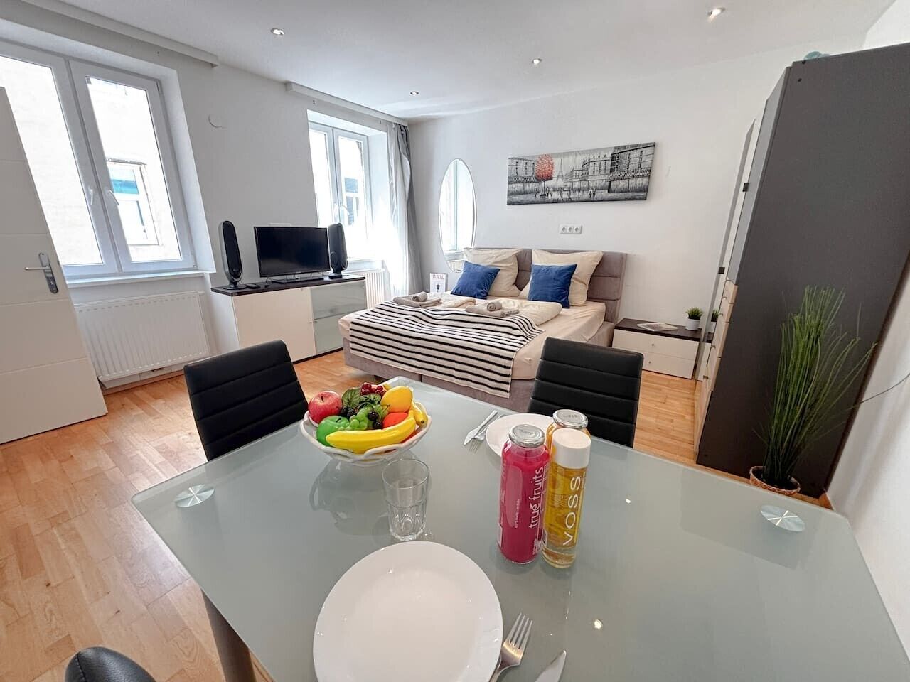 Un salon moderne avec un canapé, une table à manger ornée de fruits et de boissons, et une grande fenêtre.