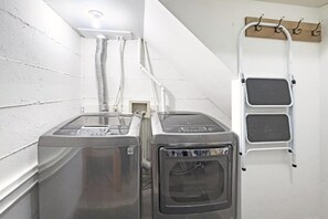 Ein Waschraum mit zwei übereinander gestapelten Waschmaschinen und Trocknern, einer Lüftungsanlage und einer Metallleiter an der Wand.