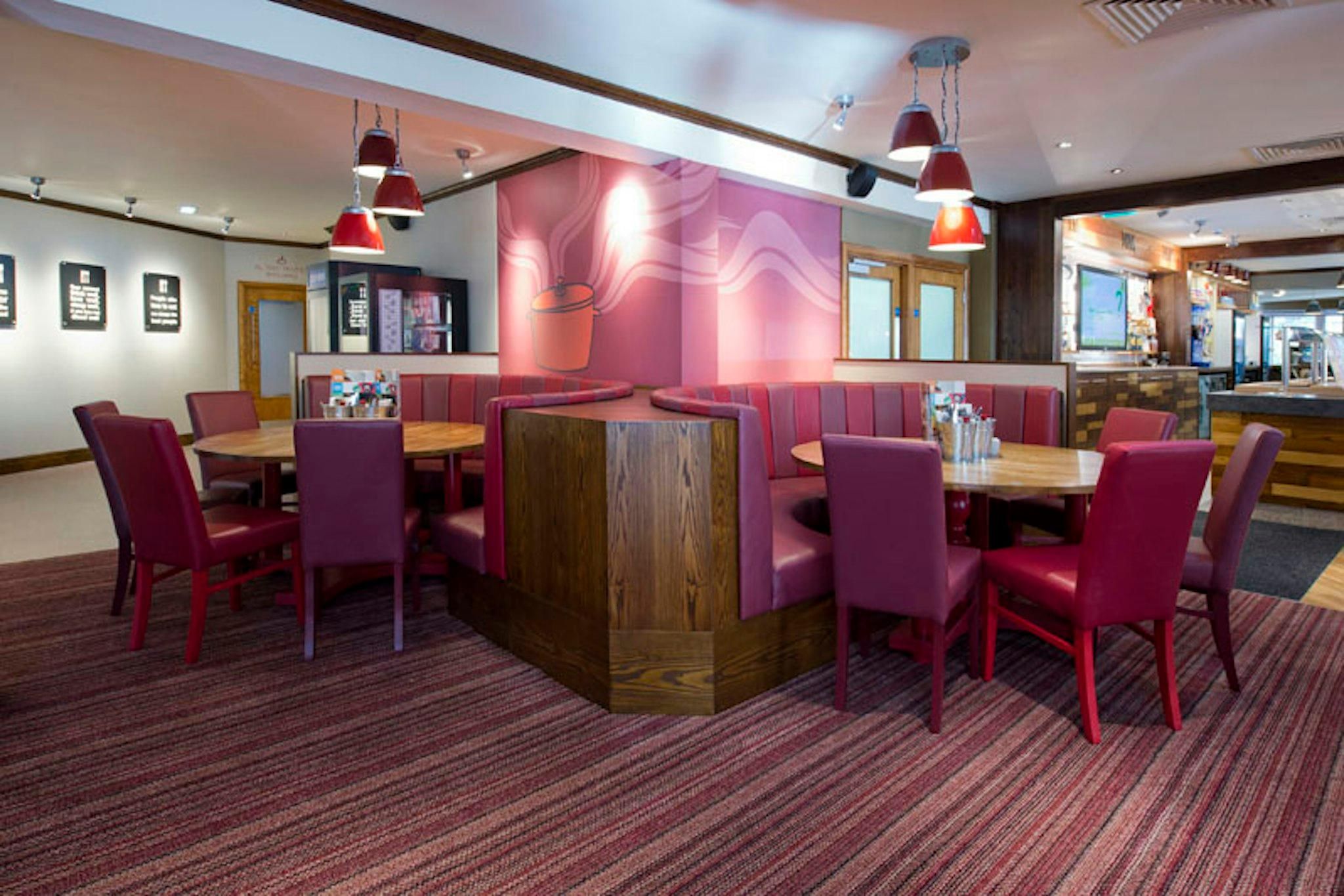 Een restaurant met zitplaatsen, tafels, rode stoelen en hanglampen.
