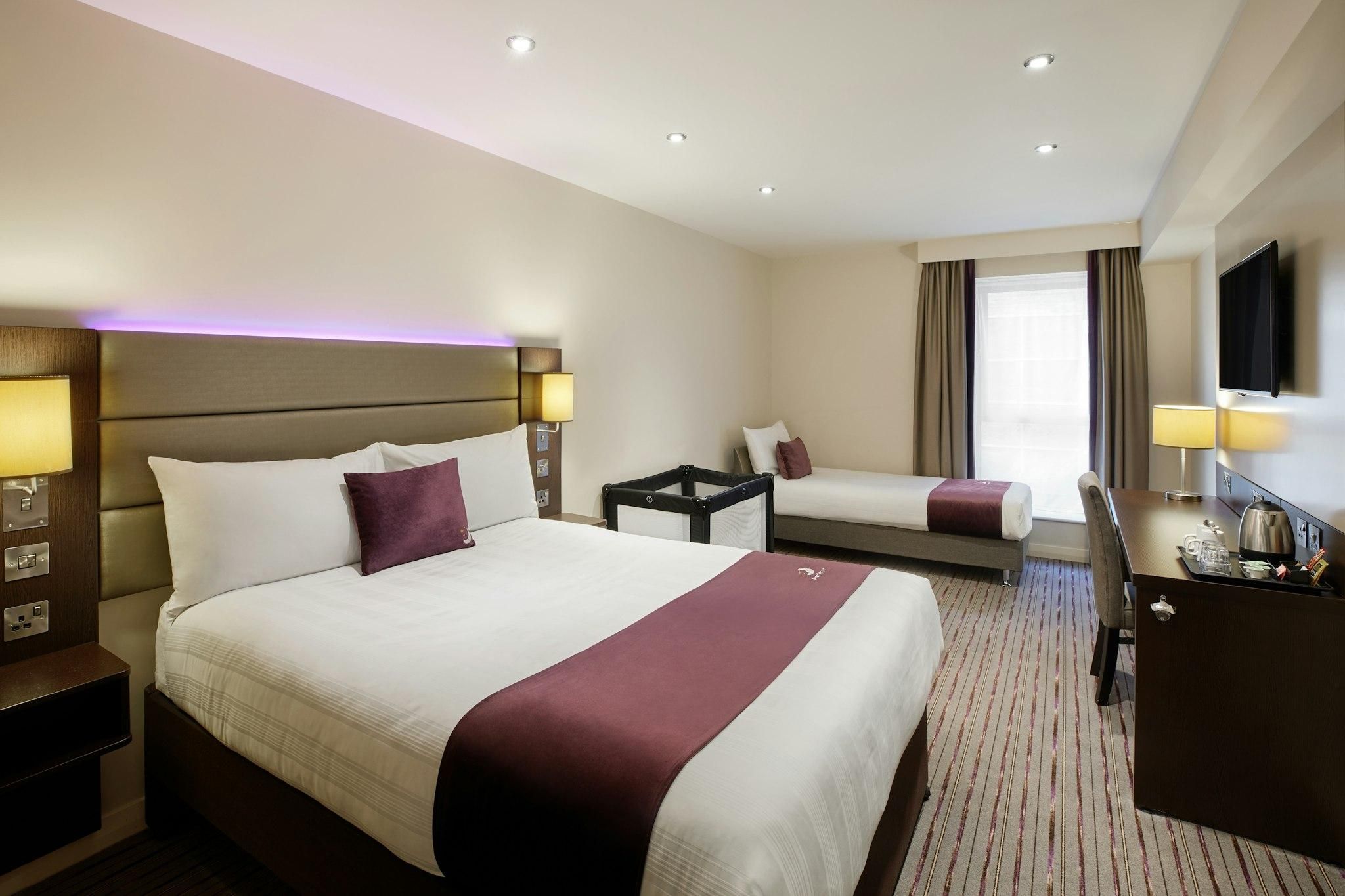 Quarto de hotel com uma cama grande, uma cama menor, uma escrivaninha e uma televisão.