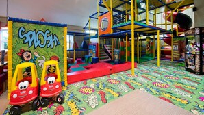 Ein Kinderspielbereich mit einer farbenfrohen Spielkonstruktion, einer Wand mit Zeichentrickfiguren und einem Boden mit Comic-Figuren.