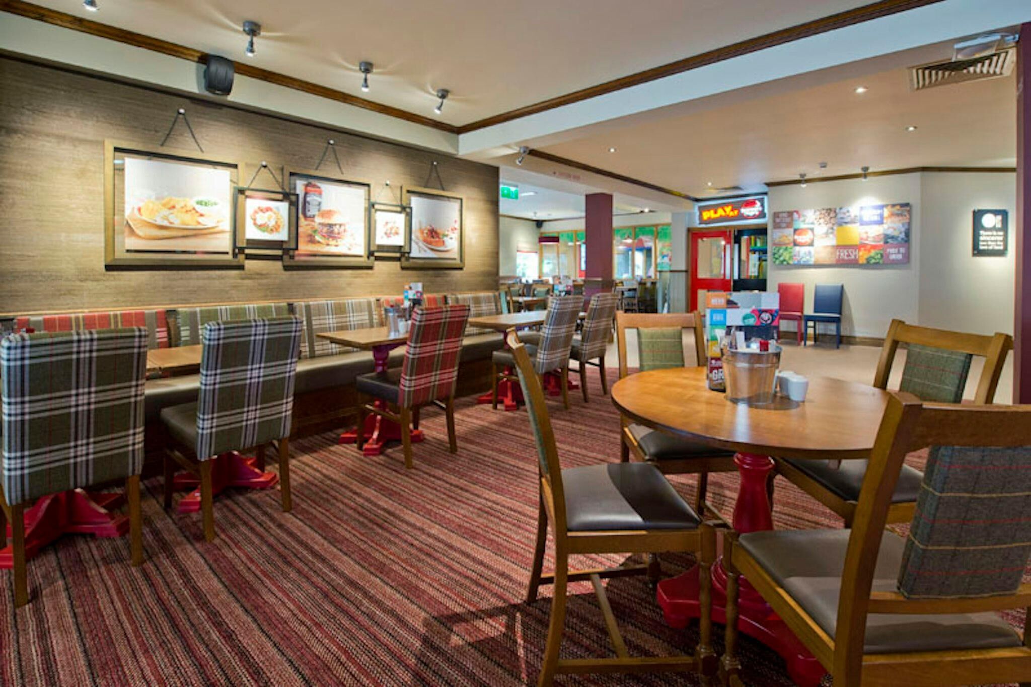 A restaurant with a red carpet, plaid chairs, and a round table.