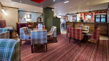 A hotel lobby with plaid-patterned seating, a bar area, and a reception desk.