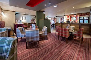 Un hall d’hôtel avec des sièges à motifs écossais, un bar et un comptoir de réception.
