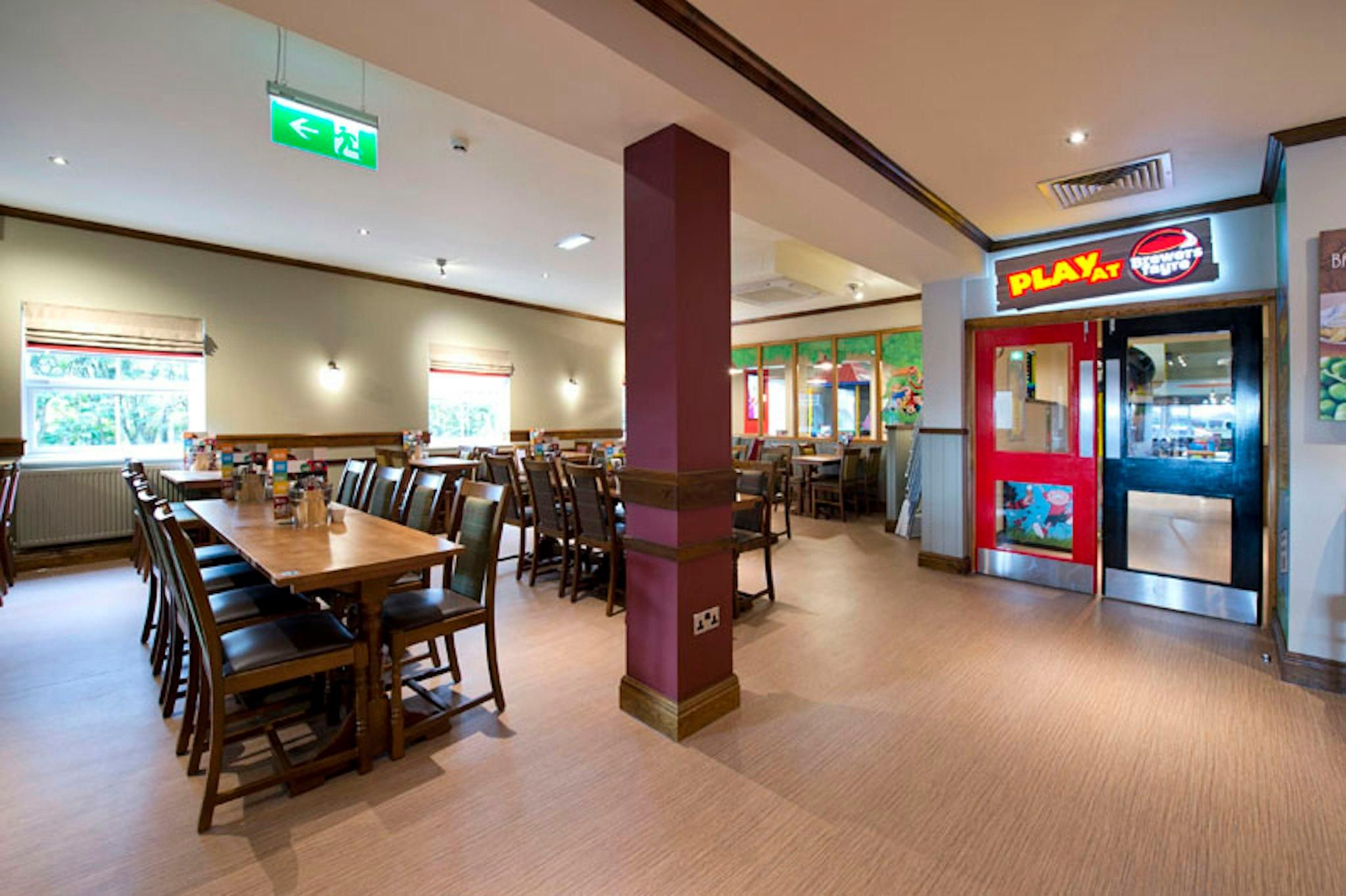 A restaurant with a long communal table and individual booths, a PlayStation sign, and a window with a view.