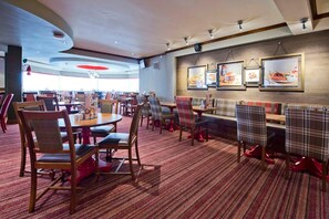 A restaurant with round tables, plaid chairs, and framed pictures on the wall. - Premier Inn Wigan (Wigan)