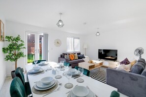 Ein modernes Wohnzimmer mit Essbereich, einer Sofagarnitur, einem Fernseher und einem Esstisch für sechs Personen.