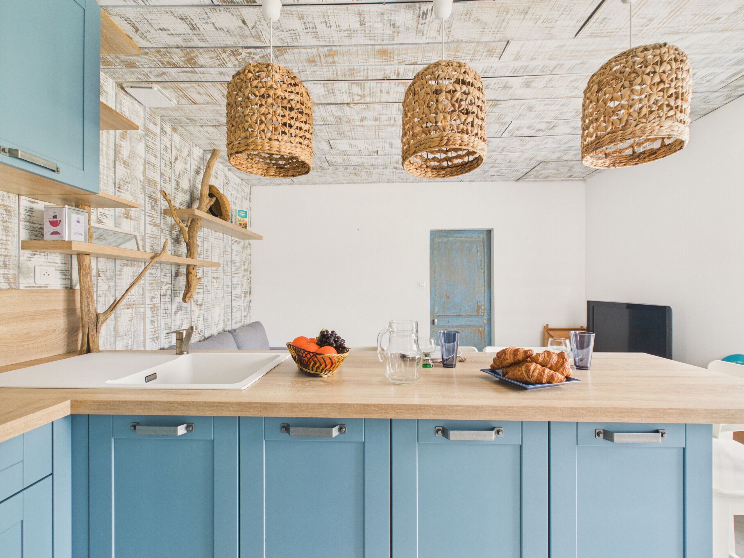 A kitchen with blue cabinets, a wooden countertop, and a hanging woven light fixture.