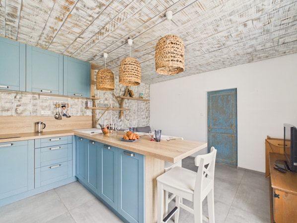 Una cocina con armarios azules, encimera de madera y cestas de mimbre colgadas.