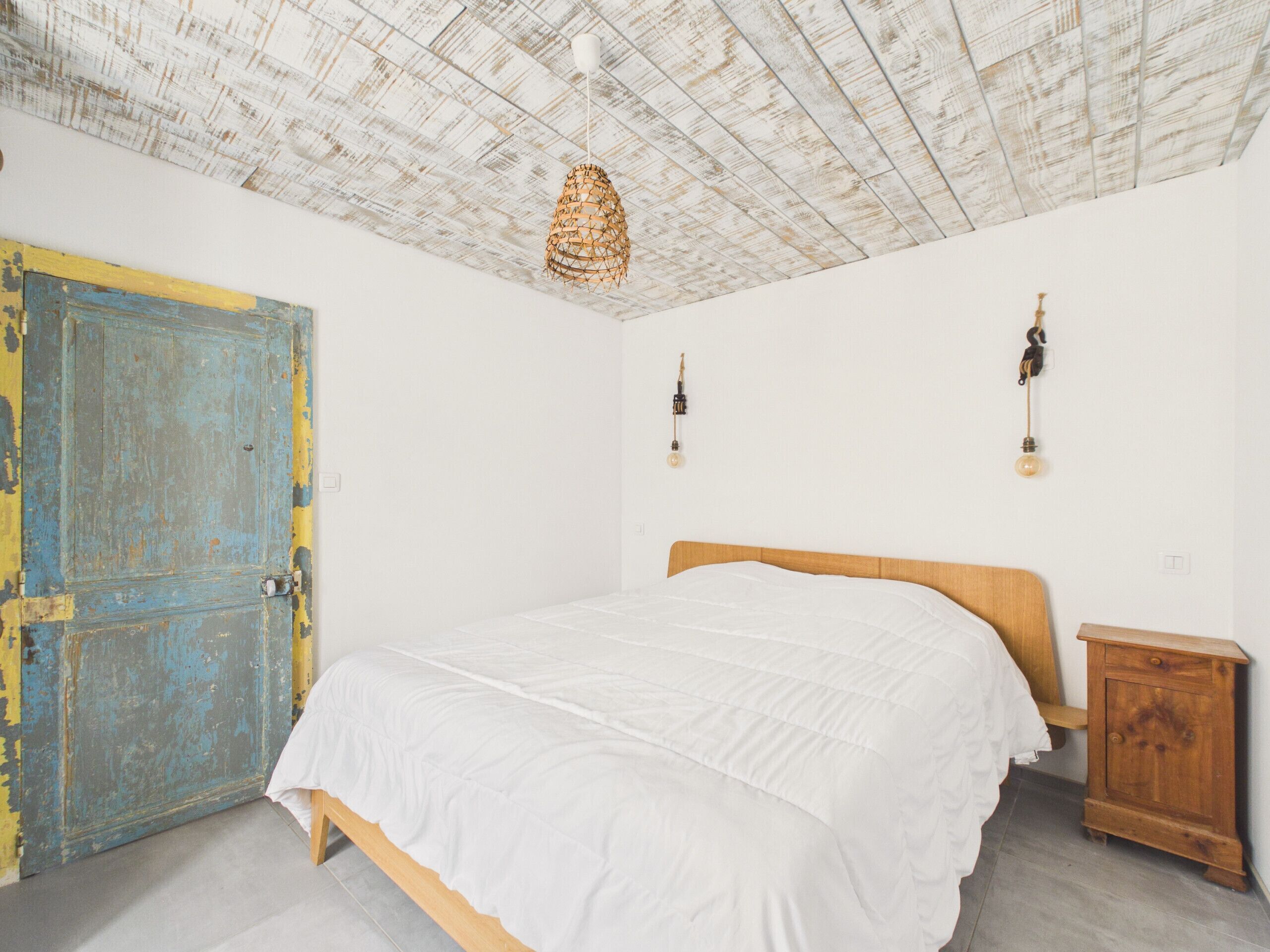 Un dormitorio con una cama de madera, una puerta azul rústica y un techo con textura.