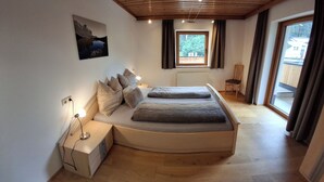 Un dormitorio con una cama curvada, una mesita de noche con lámpara, una ventana con cortinas y un cuadro en la pared.
