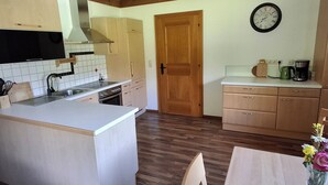 Una cocina con armarios de madera, una isla central, una estufa y un lavamanos. Hay una puerta de madera y un reloj en la pared.