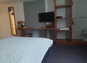 Habitación de hotel con cama, escritorio con computadora, televisión y estante con toallas.
