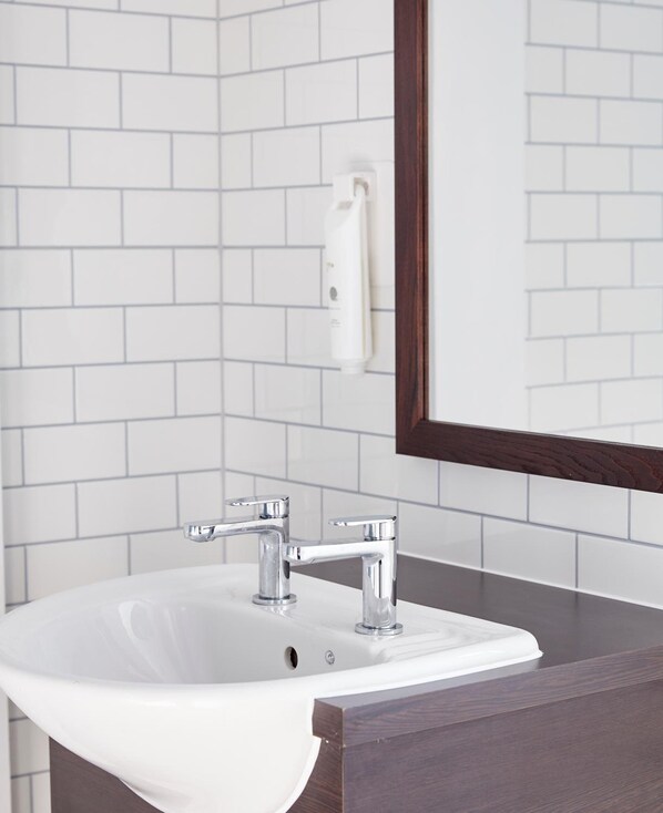 A bathroom with a white sink, two chrome faucets, a white towel dispenser, and a dark wood vanity.