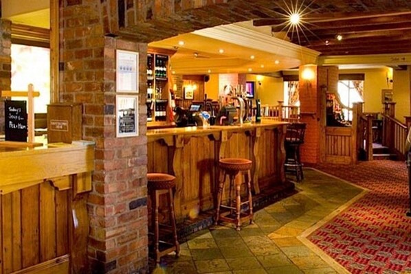 A bar area with wooden stools, a brick wall, and a counter with a menu board.