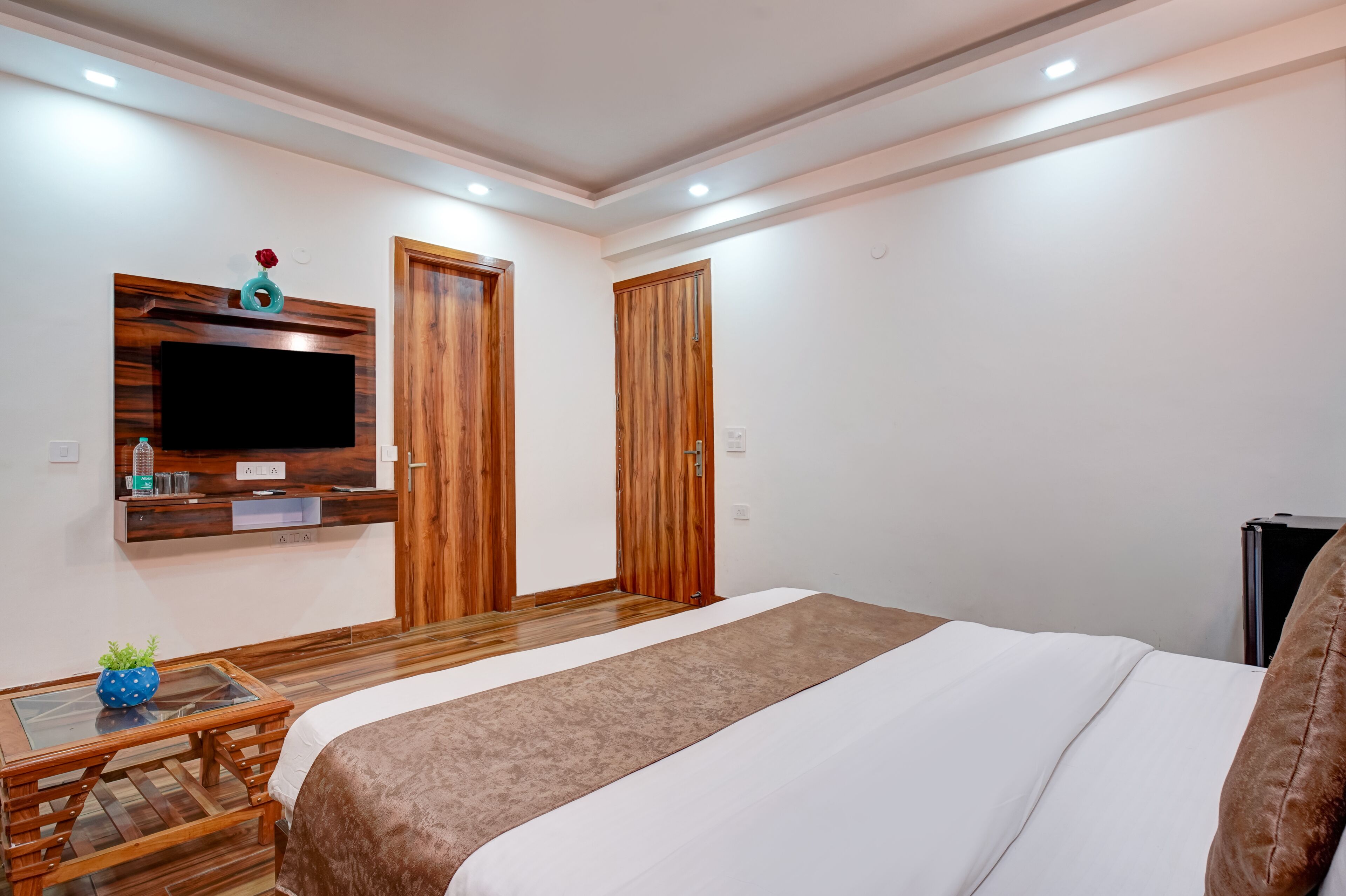 Une chambre à coucher avec un grand lit, une armoire en bois, un téléviseur fixé au mur et une petite table sur laquelle est posée une plante.