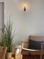 Et værelse med en træstol, en potteplante, et hvidt toilet og en vægmonteret lampe.