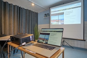 En præsentation med en bærbar computer, en projektor og et skærmbillede, der viser hotelinformation.