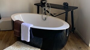 A modern bathroom with a freestanding bathtub, a small table with a vase, and a flat-screen TV mounted on the wall. - B&B Iancura (Santa Marina Salina)