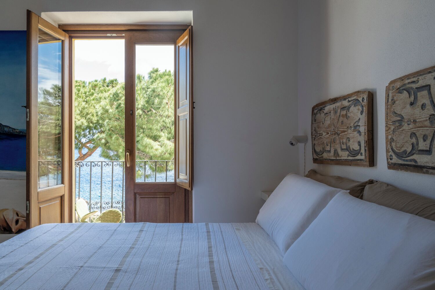 A bedroom with a bed, a door leading to a balcony, and two wall-mounted artworks.