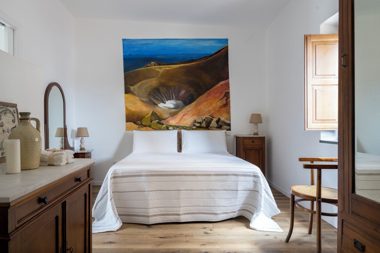A bedroom with a large bed, wooden furniture, a painting on the wall, and a view of the outdoors.