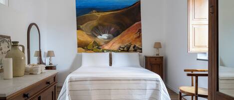 A bedroom with a large bed, wooden furniture, a painting on the wall, and a view of the outdoors.