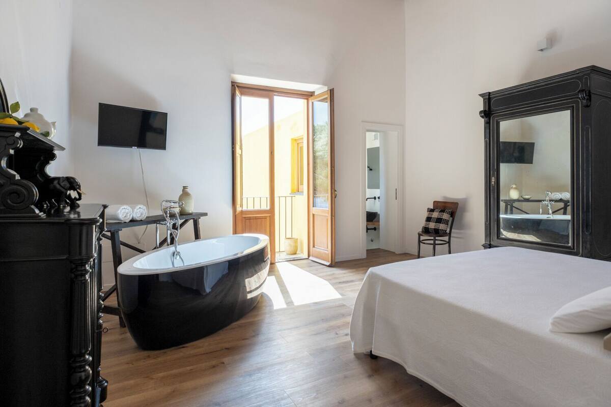 A bedroom with a large bed, a bathtub, a television, and a wardrobe.