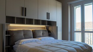 A modern bedroom with a large bed, built-in shelving, and a sliding glass door to the outside. - Eleganza Metropolitana (Turin)
