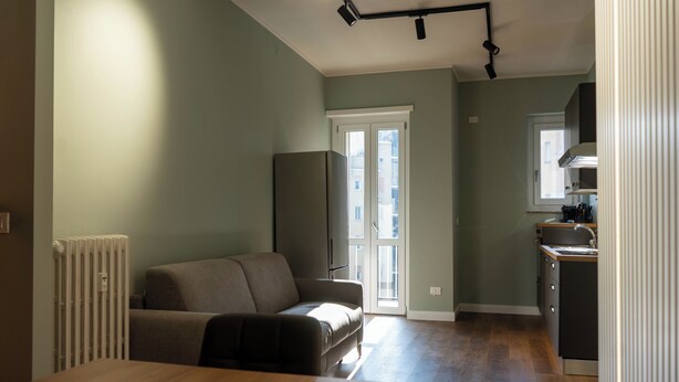 A modern living room with a sofa, a dining table, and a kitchen area with a window and cabinets. - Eleganza Metropolitana (Turin)
