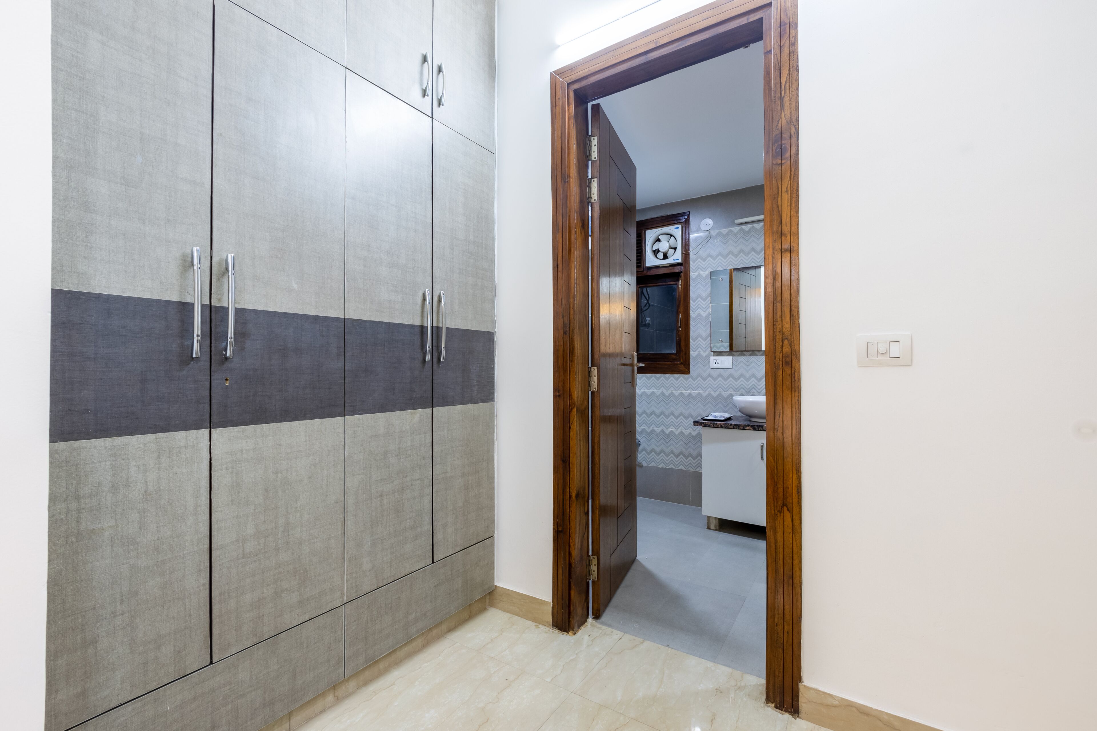 Una habitación con armario, puerta de madera y un vistazo a un baño con espejo y lavabo.