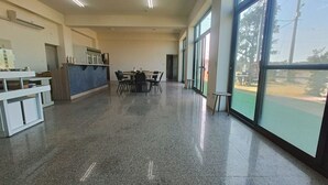 A spacious room with a polished floor, a dining area with tables and chairs, and large windows offering a view of the outdoors. - Mushrooms (Jinning)