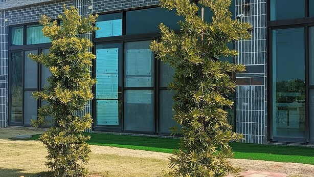 A modern building with a brick facade and large windows. There is a small outdoor seating area with a table and chairs. - Mushrooms (Jinning)