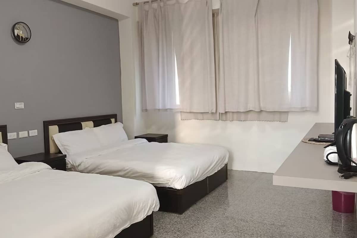 Habitación de hotel con dos camas, un escritorio con hervidor y una ventana con cortinas.