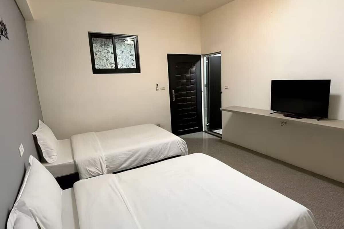 Un dormitorio con dos camas individuales, un televisor en un estante y una puerta que da a otra habitación.