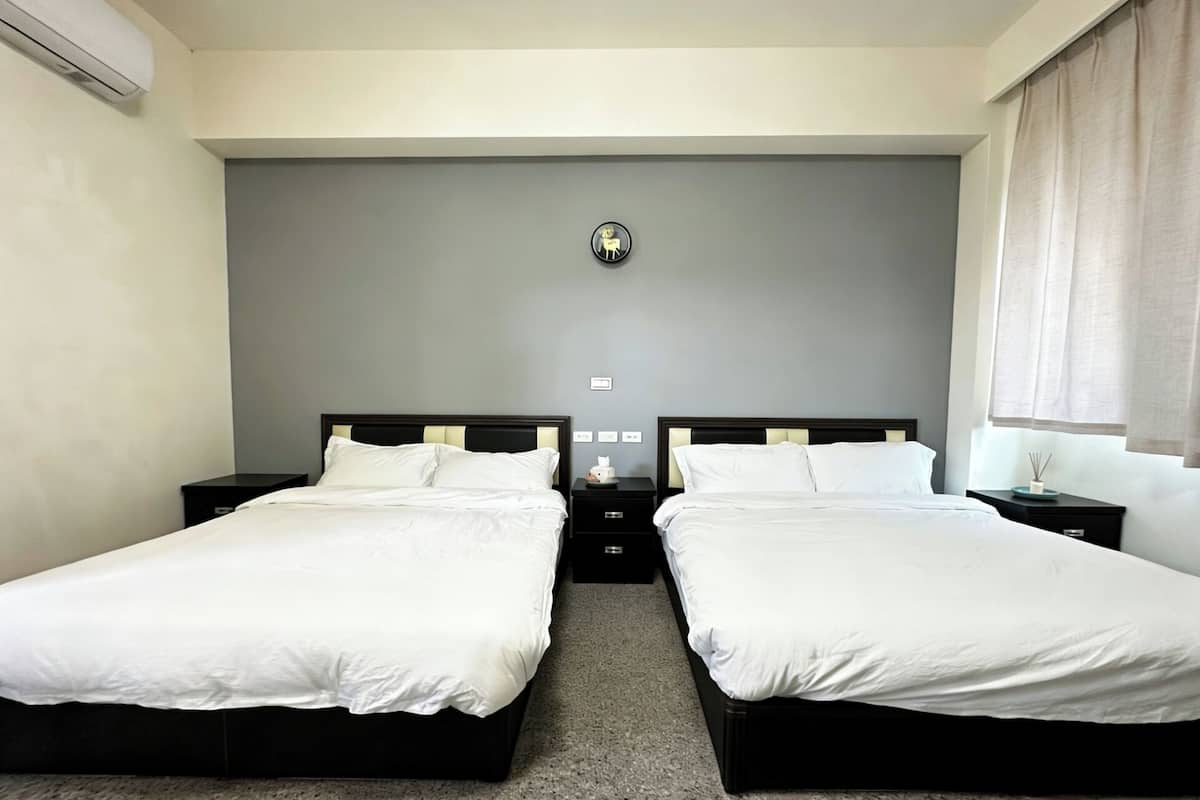Una habitación doble con dos camas, un muro de acento gris, un reloj de pared pequeño y una ventana con cortinas.