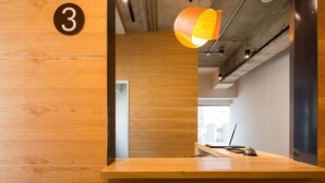 Un comptoir d’accueil en bois, orné d’un panneau portant le chiffre « 3 », une lampe suspendue et une vue sur l’extérieur à travers une porte vitrée.