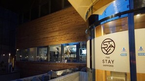 Il s’agit d’un bâtiment moderne doté d’une façade en bois et d’une entrée en verre. À l’intérieur, on peut voir une enseigne indiquant le restaurant « The Stay Sapporo ».