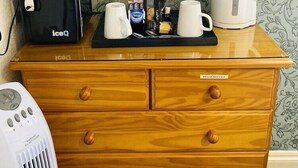 Une commode en bois sur laquelle sont posés un sèche-cheveux, un grille-pain noir de la marque iceQ et une bouilloire blanche.