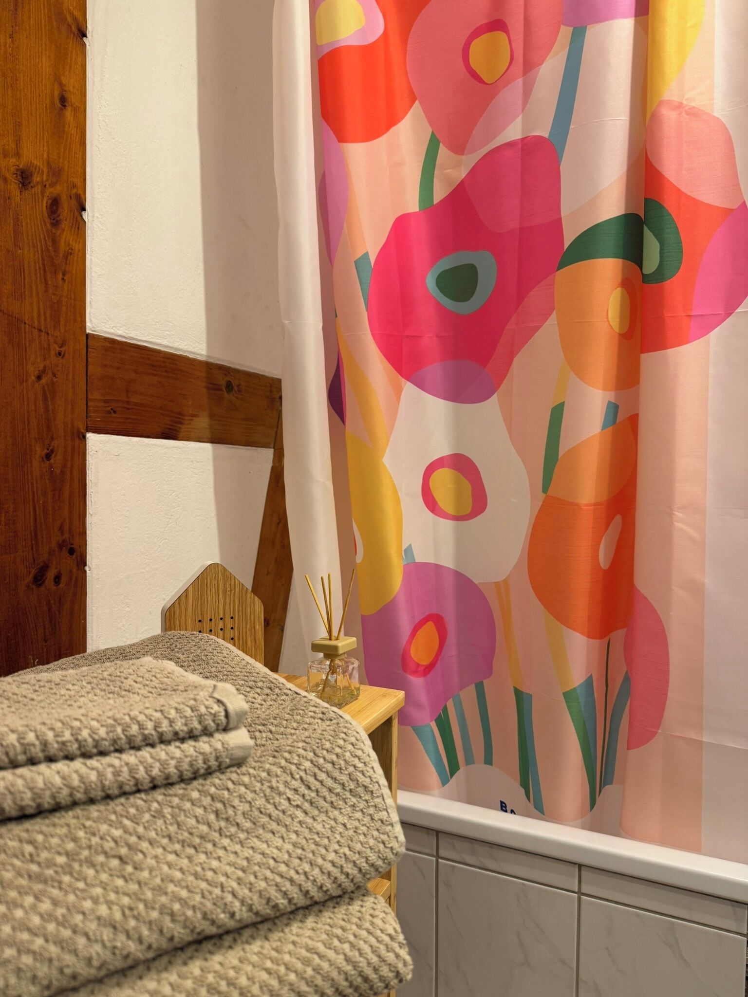 Quarto com cabeceira de madeira, manta tricotada bege e cortina de chuveiro abstrata e colorida.