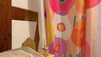 Quarto com cabeceira de madeira, manta tricotada bege e cortina de chuveiro abstrata e colorida.
