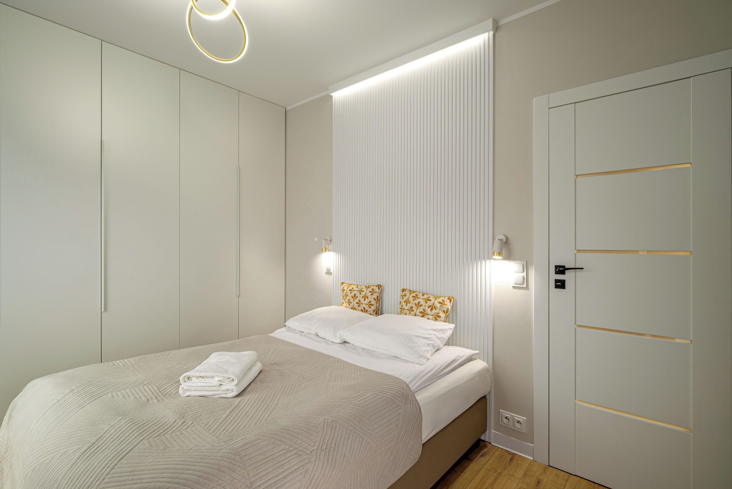 A bedroom with a bed, bedside lamps, a wardrobe, and a door.