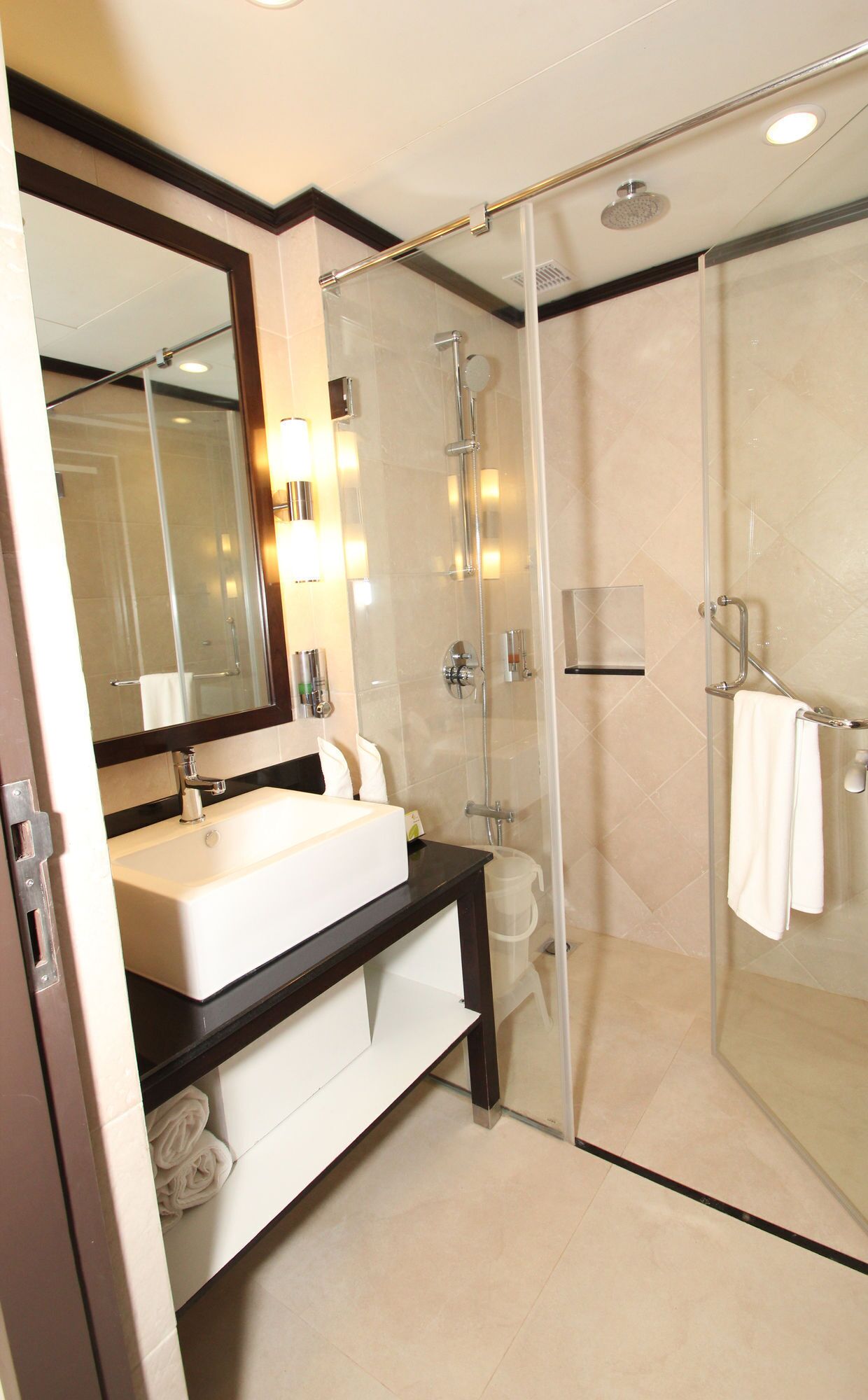 A modern bathroom with a glass-enclosed shower, a large mirror, and a vanity with a sink and towel rack.