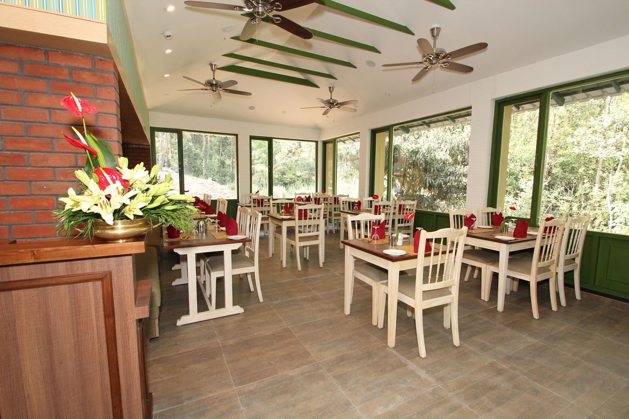 A restaurant with multiple tables and chairs, ceiling fans, and large windows offering a view of the outdoors.