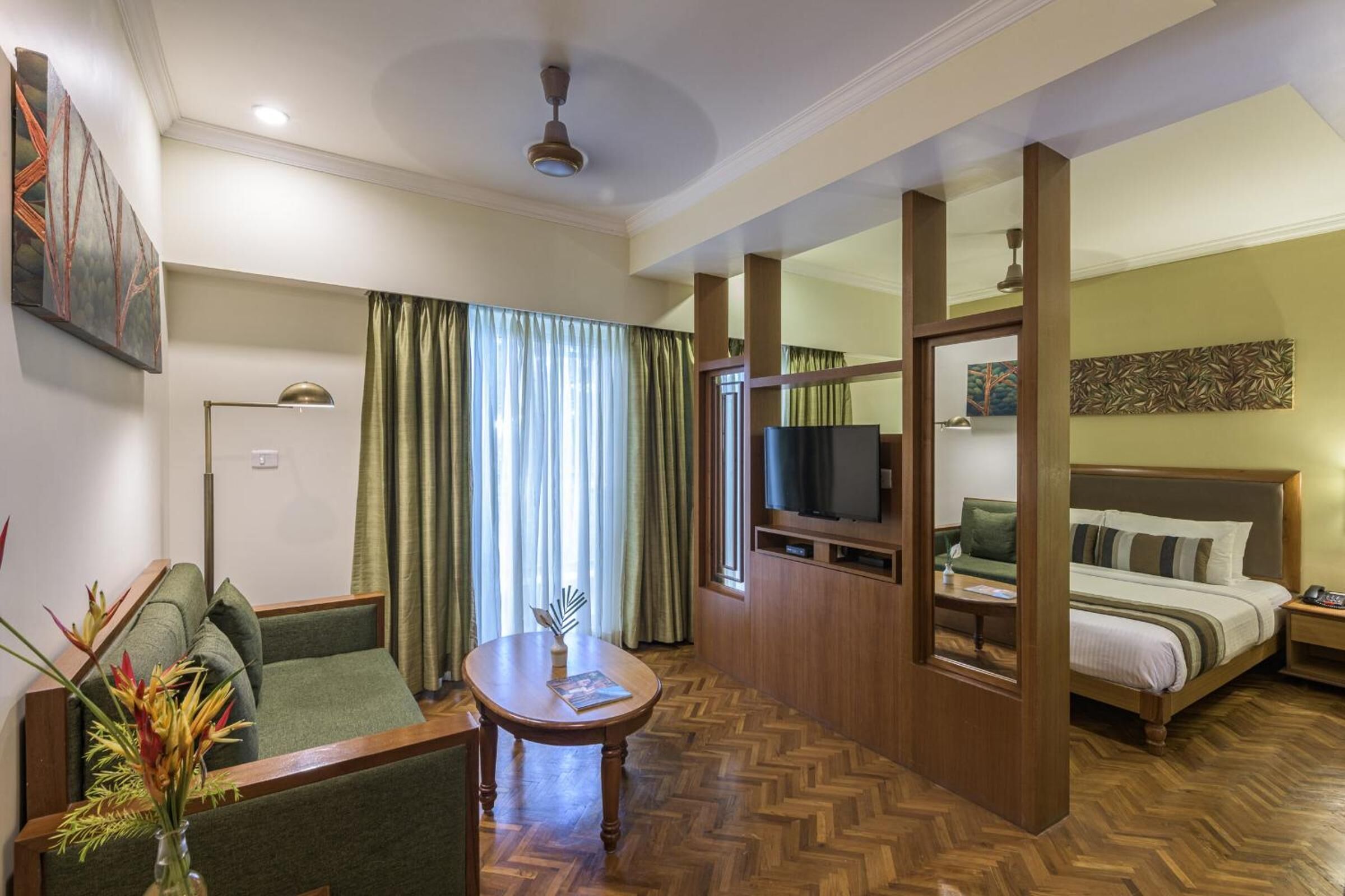 Una habitación de hotel con sofá, una mesita, televisor, cama y un adorno en la pared.