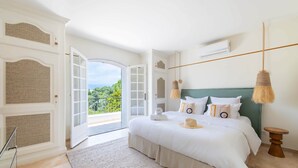A bedroom with a large bed, a view through an open door, and a hanging lamp. - Villa Anna on the Côte d'Azur | 8 bedrooms, private Padel and P (Valbonne)