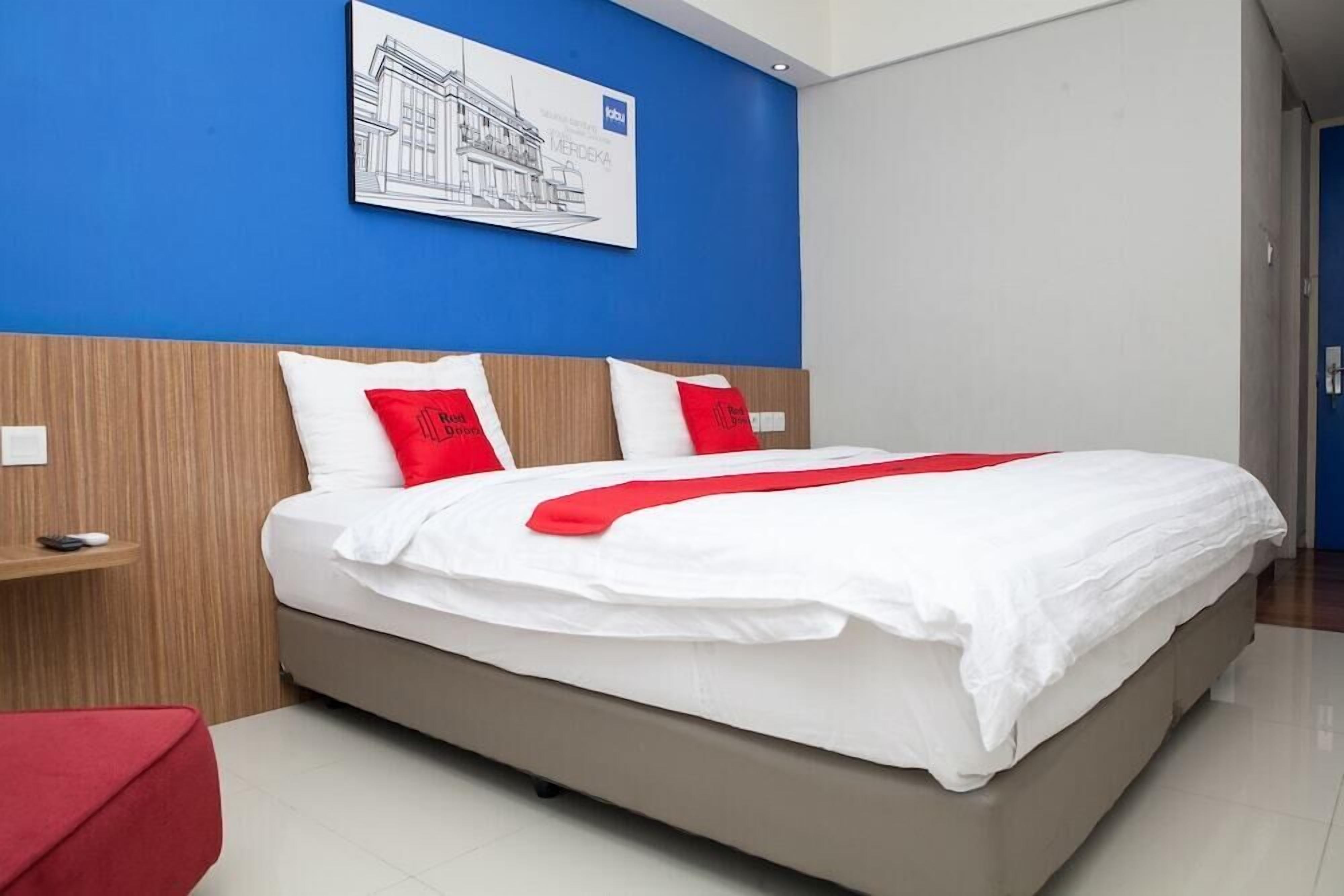A modern hotel room with a large bed, red and white bedding, a wooden headboard, and a blue accent wall.