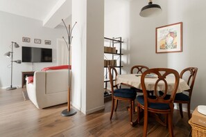 Una sala de estar con un sofá, una mesa de comedor con sillas, una estantería, un televisor y una lámpara.
